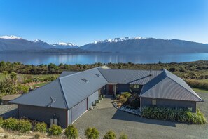 A modern building with a sloped roof, a covered driveway, and a view of a lake and mountains in the background. - Loch Vista Lake View Villa Accommodation (Te Anau)
