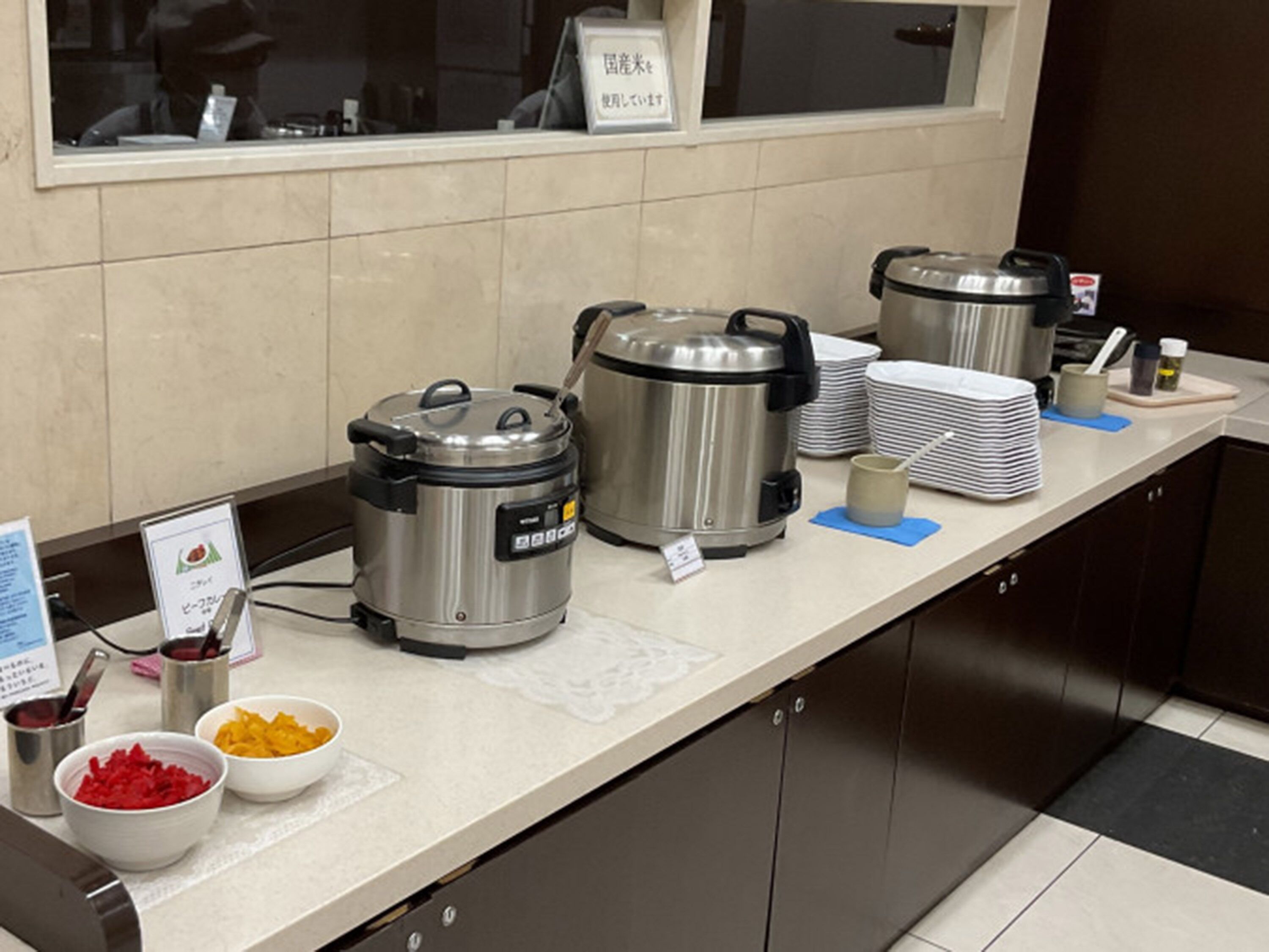 A buffet setup with multiple food containers, a stack of plates, and serving utensils.