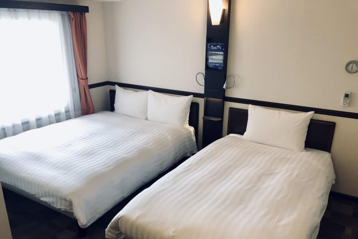 A hotel room with two single beds, a nightstand, a wall-mounted TV, and a clock.