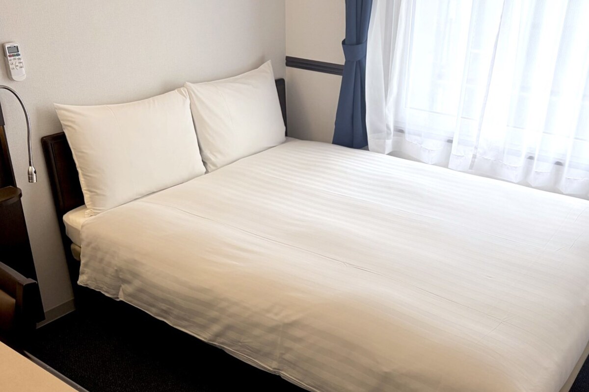 Une chambre d’hôtel avec un grand lit, une table de chevet, une lampe et une fenêtre avec des rideaux.