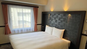 Een hotelkamer met een groot bed, een hoofdeinde met een geometrisch patroon, een raam met dunne gordijnen en een aan de muur bevestigd toestel.