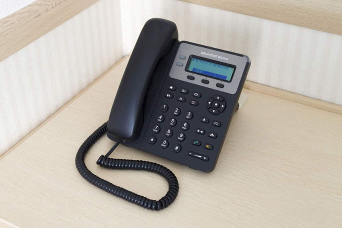 A black telephone with a keypad and a small screen, placed on a wooden surface.