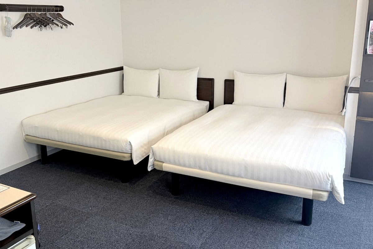 Une chambre d’hôtel avec deux lits simples, une petite table et un porte-manteau avec des cintres.