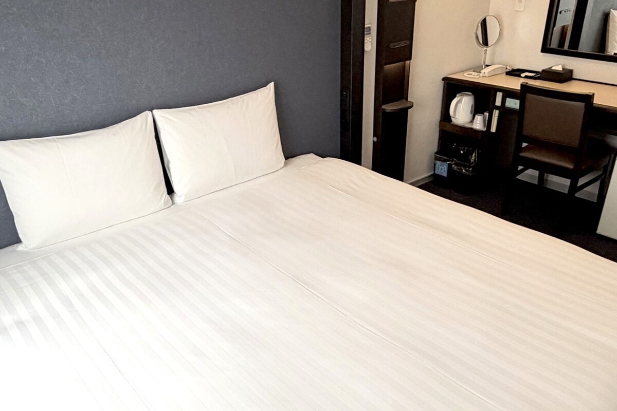 Une chambre d’hôtel équipée d’un lit, d’un bureau, d’une chaise, d’un miroir et d’un téléphone.