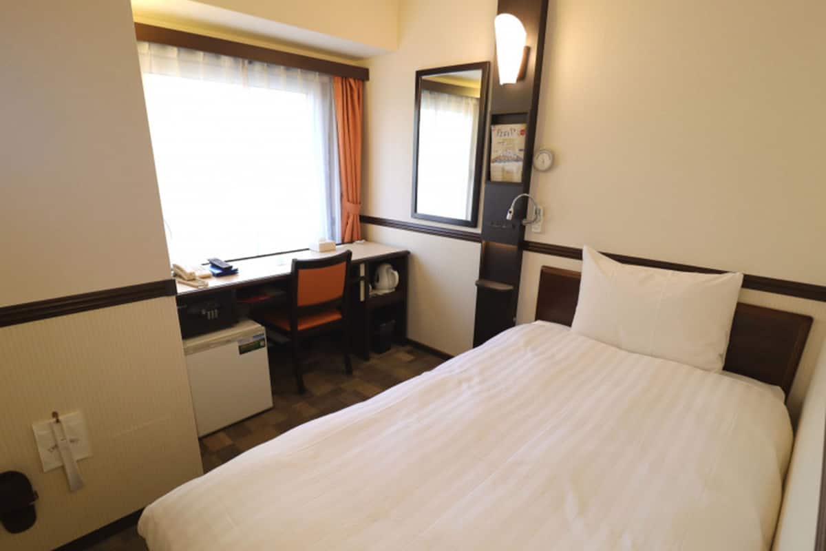 A hotel room with a bed, a desk, a chair, a microwave, and a small refrigerator.
