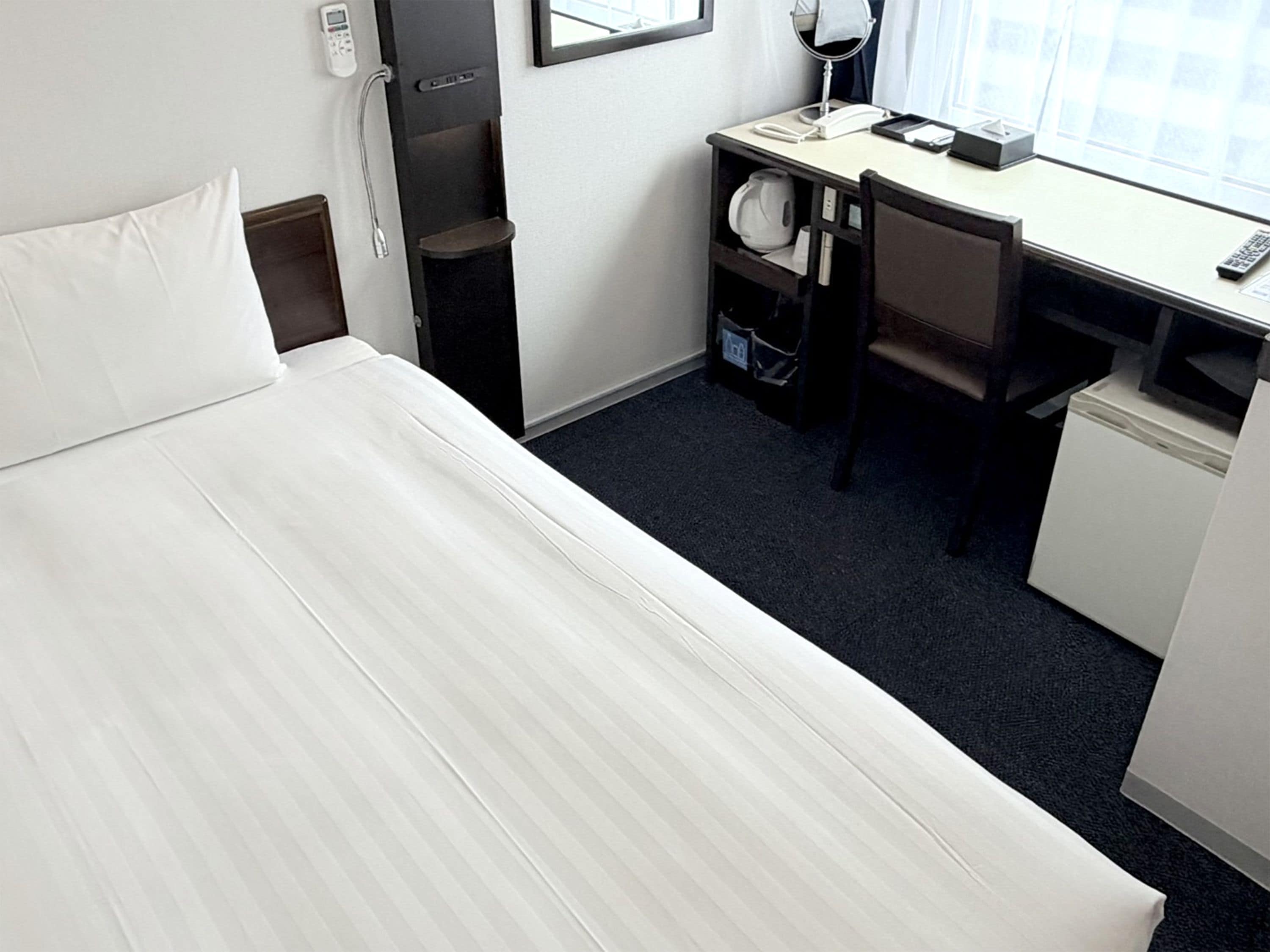 Una camera d'albergo con un letto, una scrivania, una sedia e un piccolo frigorifero.