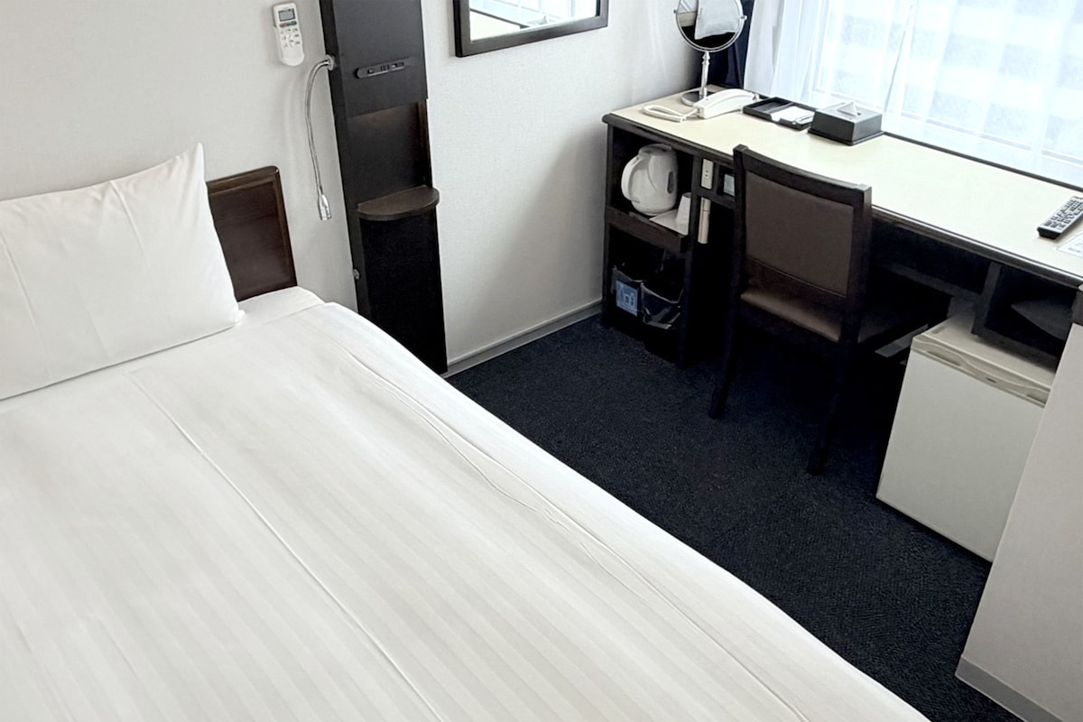 Une chambre d’hôtel équipée d’un lit, d’un bureau, d’une chaise et d’un petit réfrigérateur.