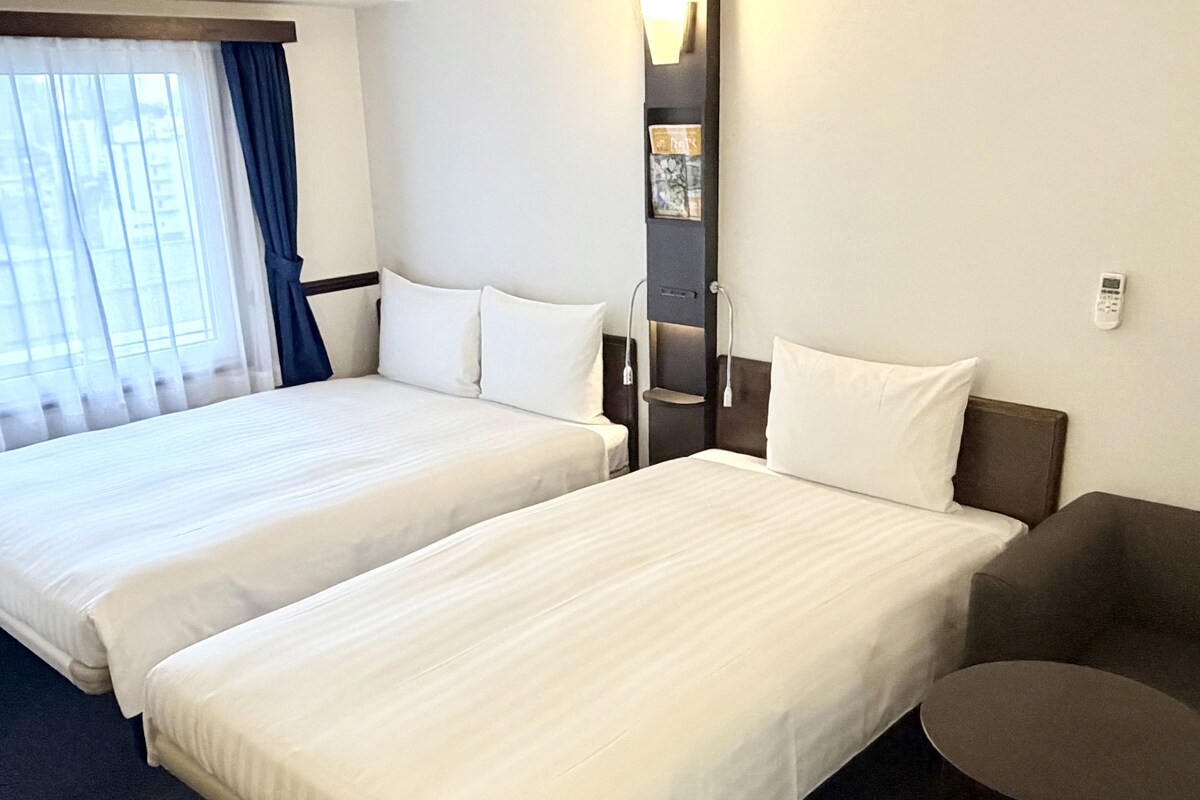 Une chambre d’hôtel avec deux lits, une petite table et une fenêtre avec des rideaux.