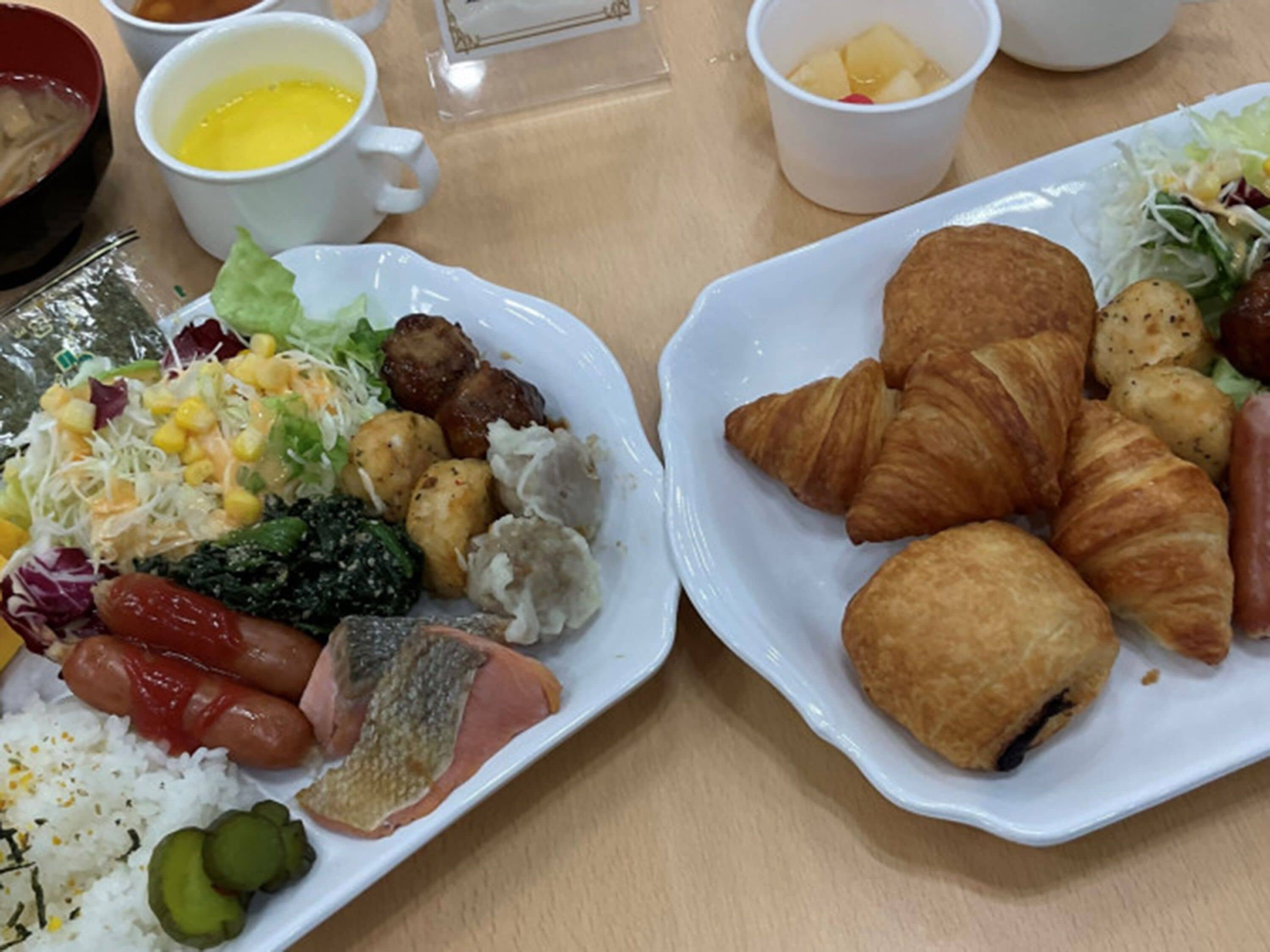 Una mesa de desayuno con platos de comida, incluyendo cruasanes, salchichas y una ensalada.
