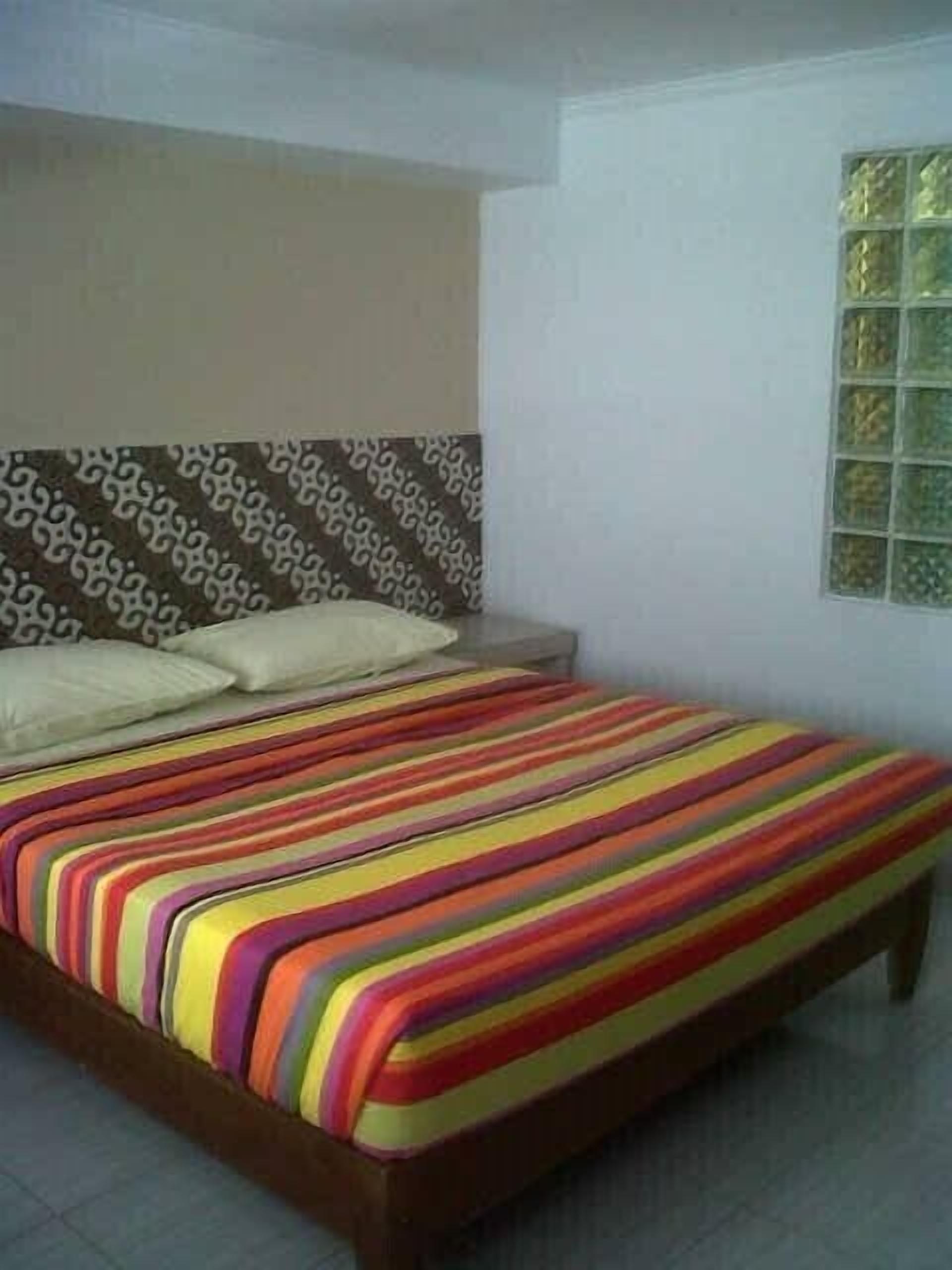 A bed with a colorful striped bedspread in a room with a patterned headboard and a window with a decorative grid.