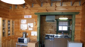 A compact kitchen with wooden cabinets, a microwave, a stove, and a refrigerator. - Cottage Primal Stage (Kamishihoro)