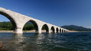 A large stone bridge with multiple arches spanning a body of water, surrounded by a natural landscape. - Cottage Primal Stage (Kamishihoro)
