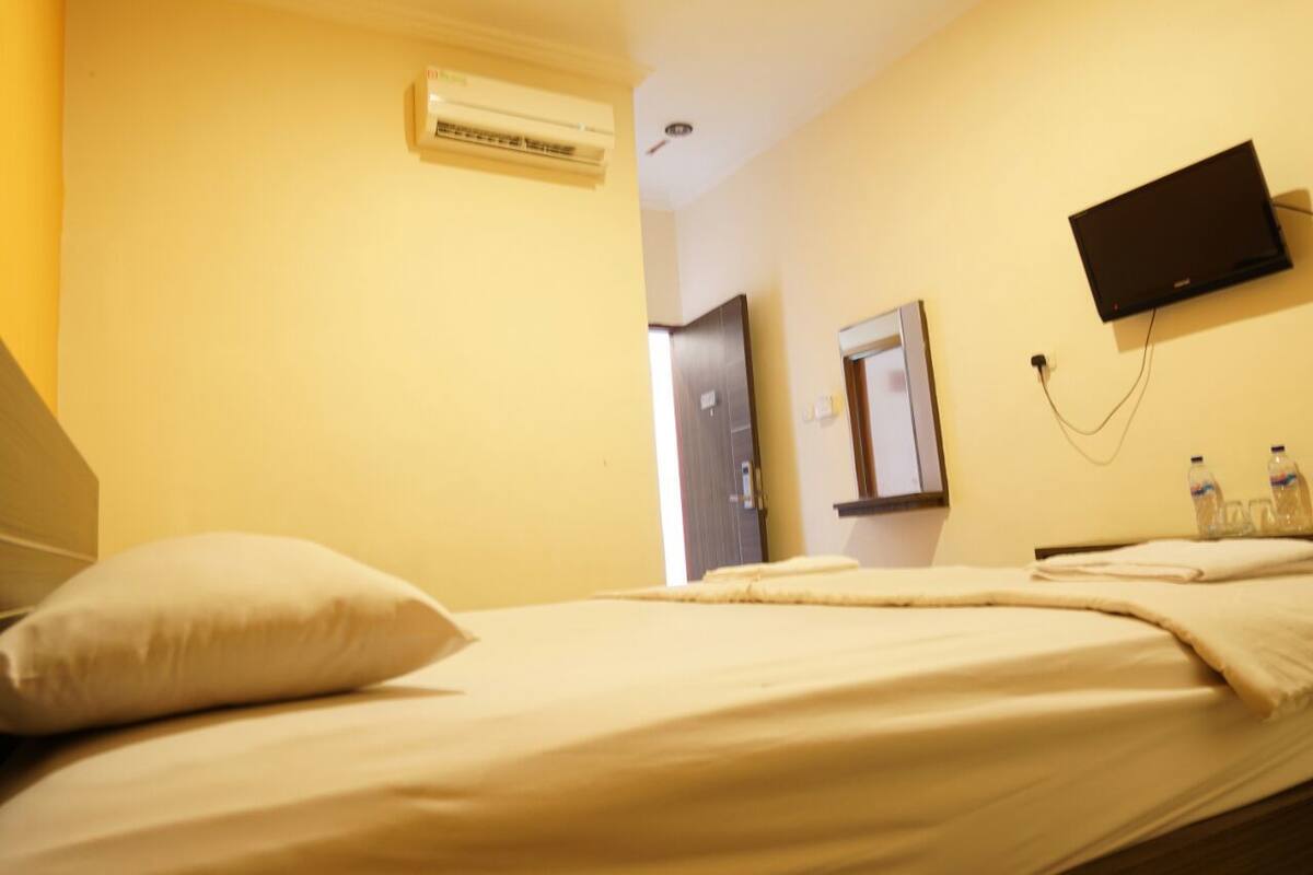 Quarto de hotel com uma cama, aparelho de ar condicionado, televisão montada na parede e uma porta.