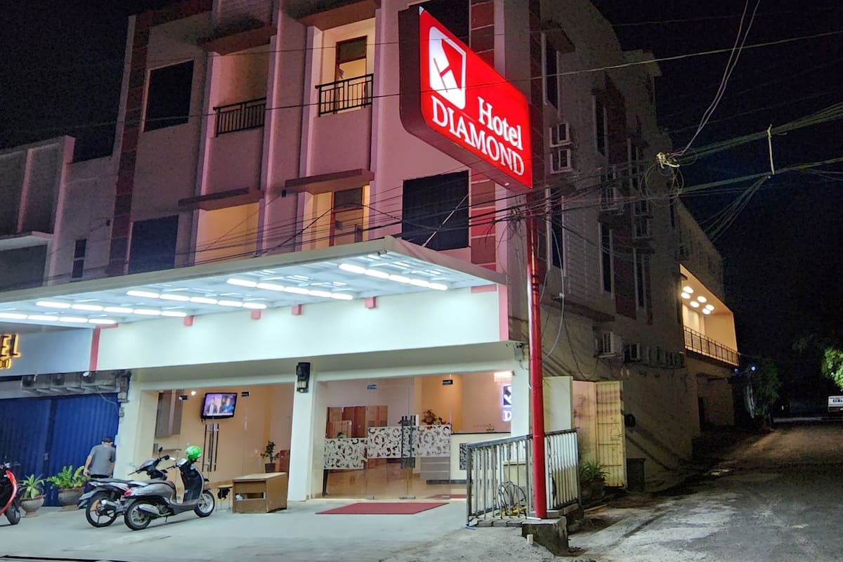 Um hotel com uma placa visível, entrada coberta e alguns scooters estacionados.