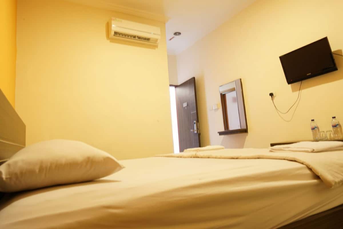 Quarto de hotel com cama, ar condicionado, televisão e porta.