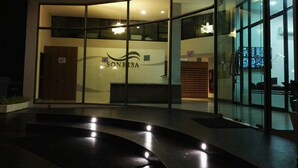 A modern building with a glass facade, a reception area with a sign reading "SONRISA," and a curved black floor leading to the entrance. - Sonrisa Sriracha (Si Racha)