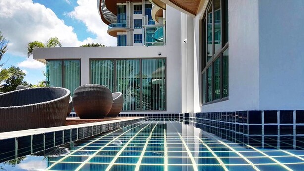 A modern pool area with clear blue tiles and a view of a contemporary building with large windows and a unique architectural feature. - Sonrisa Sriracha (Si Racha)