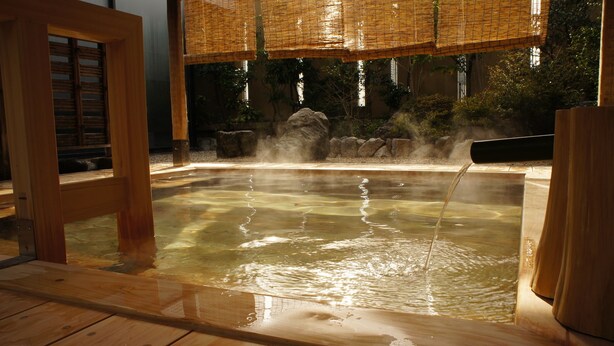 A hot spring area with wooden flooring and a stone wall in the background. - Yukeikohan Suitenkaku (Matsue)