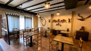 A dining area with wooden tables and chairs, a fireplace, and wall-mounted kitchen utensils. - Casa Rural Los Garridos (Casas Bajas)