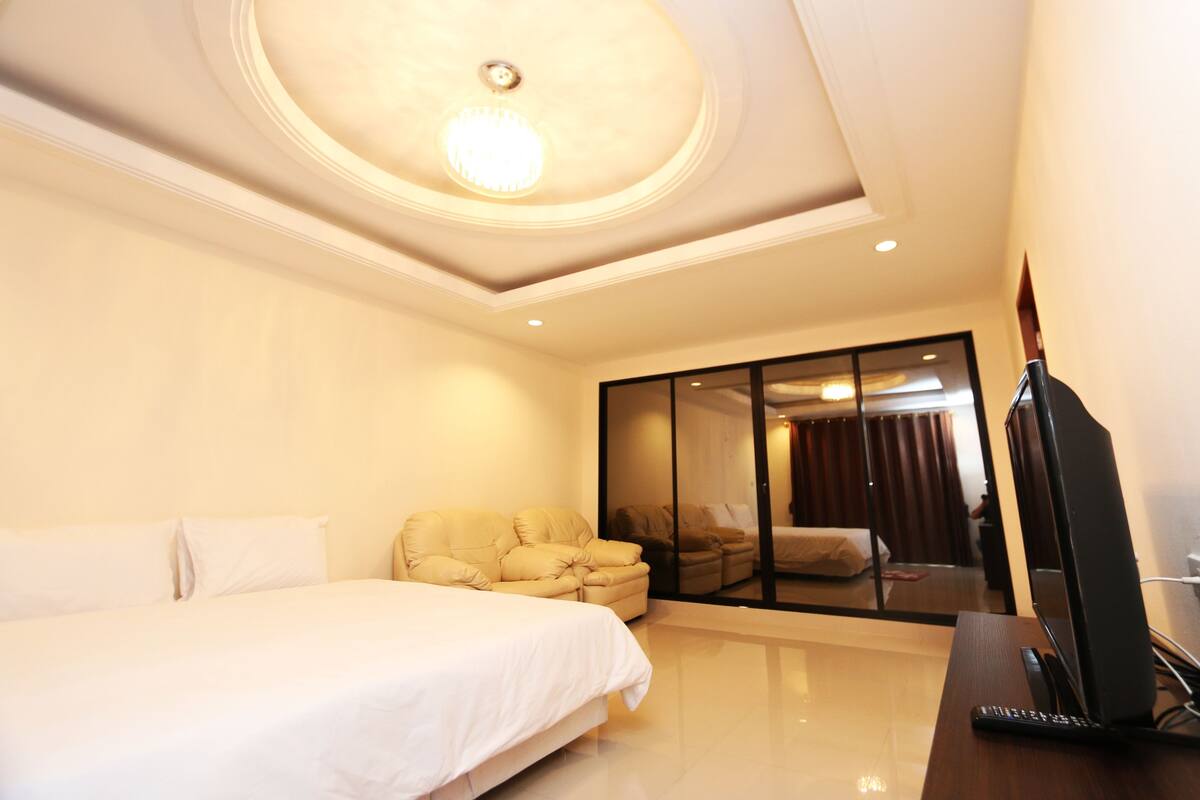 A hotel room with a bed, a sofa, a TV, and a large window.