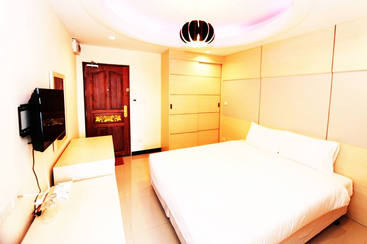 A hotel room with a bed, a desk, a television, and a wardrobe.