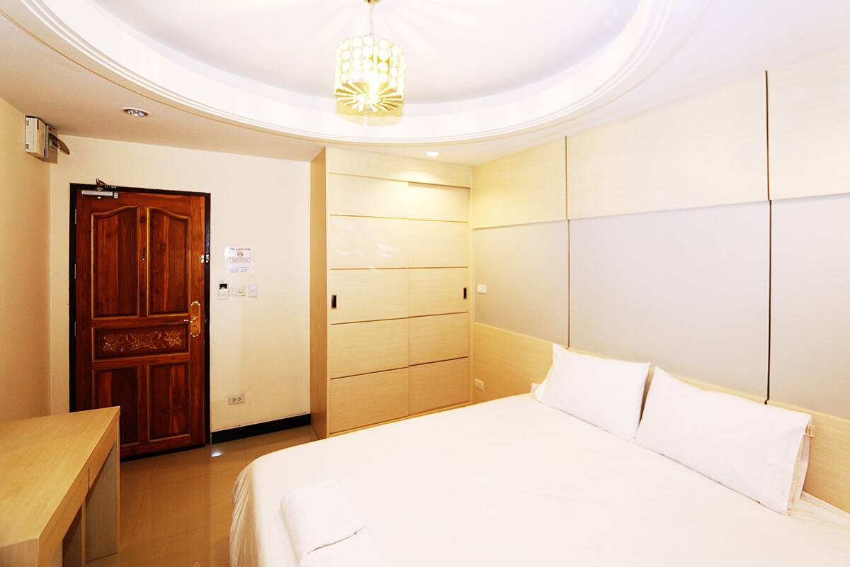 A hotel room with a wooden door, a bed with white linens, a wooden wardrobe, and a ceiling light fixture.