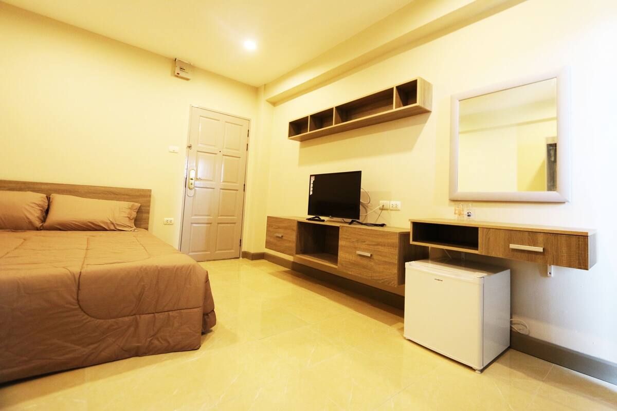 A bedroom with a bed, a TV, a small fridge, and a wardrobe.