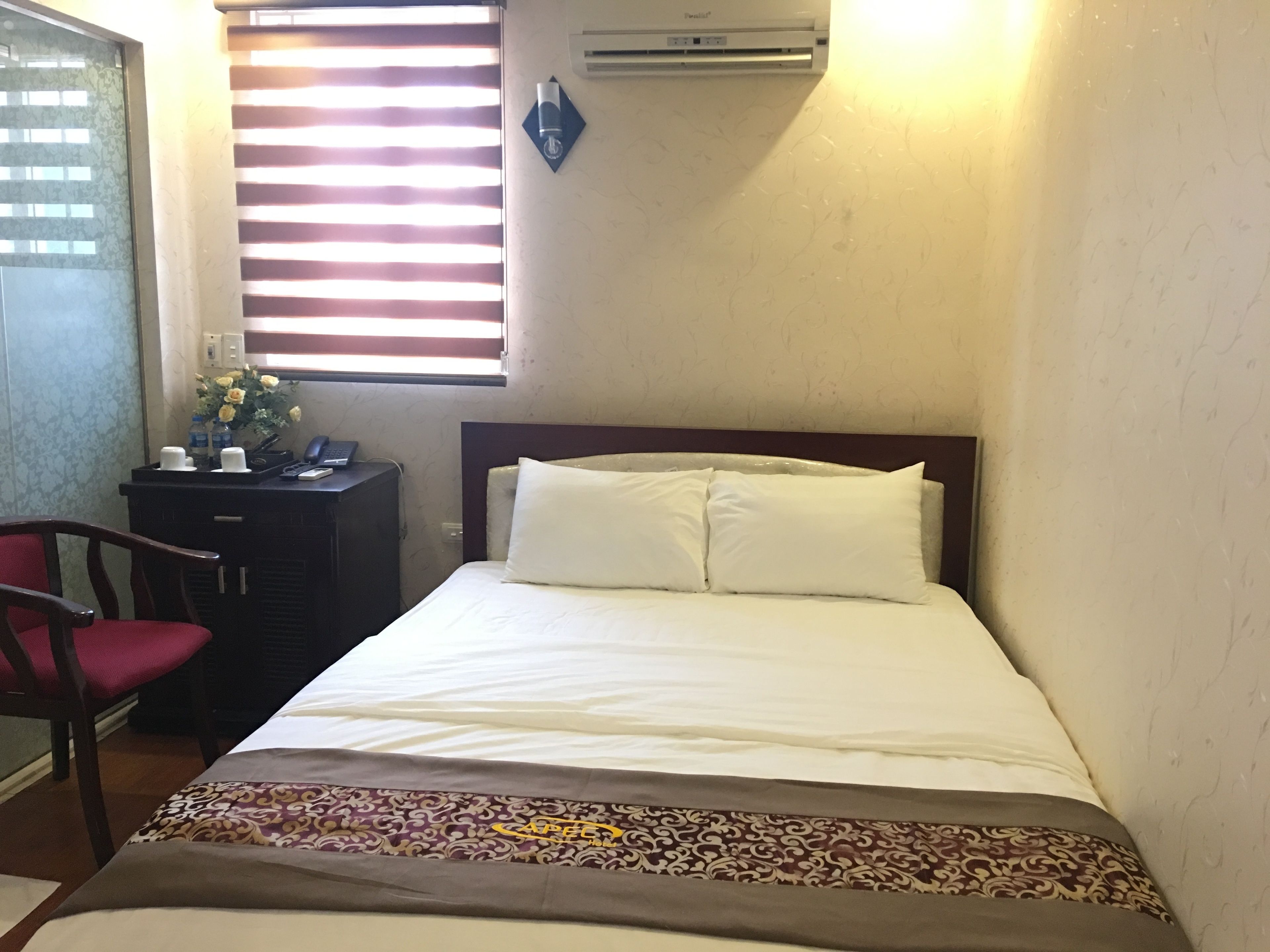 Una habitación de hotel con cama, escritorio, silla y ventana con persianas.