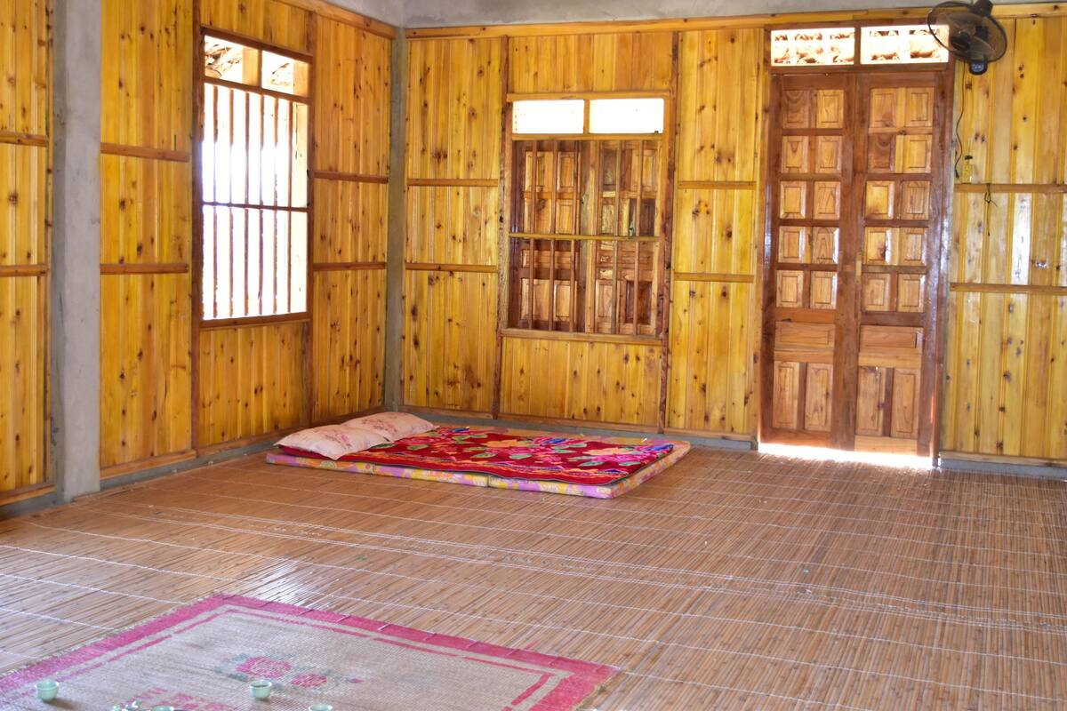 A room with wooden walls, a bed with a colorful blanket, and a window with bars.