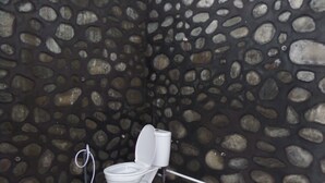 A bathroom with a stone wall, a white toilet, and a visible pipe. - Losmen Adas (Ngadisari)