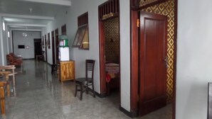 A hallway with a wooden door, a chair, a small table, and a refrigerator. - Losmen Adas (Ngadisari)