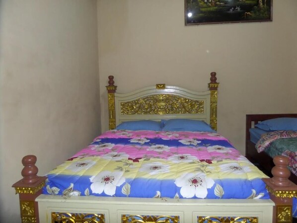 A bed with a floral bedspread, a headboard with intricate designs, and a painting on the wall. - Losmen Adas (Ngadisari)
