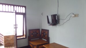 A room with a wooden table, two wooden chairs, a television mounted on the wall, and a window with blinds. - Losmen Adas (Ngadisari)