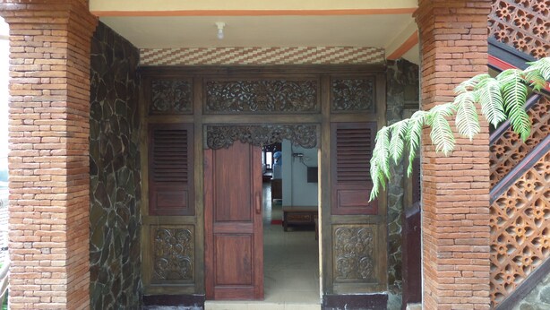 A traditional entrance with a wooden door and intricate carvings, brick walls, and a decorative metal grille. - Losmen Adas (Ngadisari)