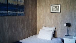 A hotel room with a wooden panel wall, a bed with white linens, a framed picture on the wall, and a bedside lamp.