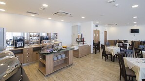 A hotel dining area with a buffet, seating, and a coffee station.