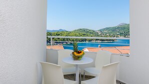 A balcony with a table and chairs, a fruit bowl, and a scenic view of a coastal area with mountains and a beach.