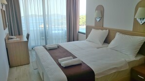 A hotel room with a bed, a desk, a lamp, and a view of the sea.