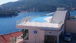 A rooftop pool with a glass balustrade, a parking sign, and a view of the sea and hills.