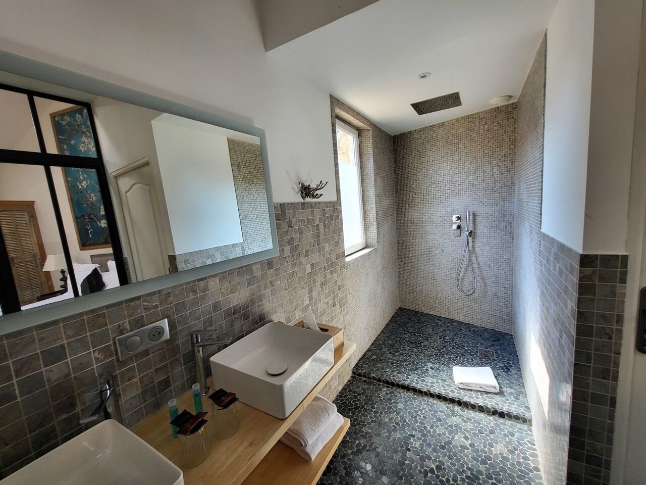 Ein modernes Badezimmer mit einem großen Spiegel, einem rechteckigen Waschbecken, einer Duschkabine und einem kleinen Fenster.