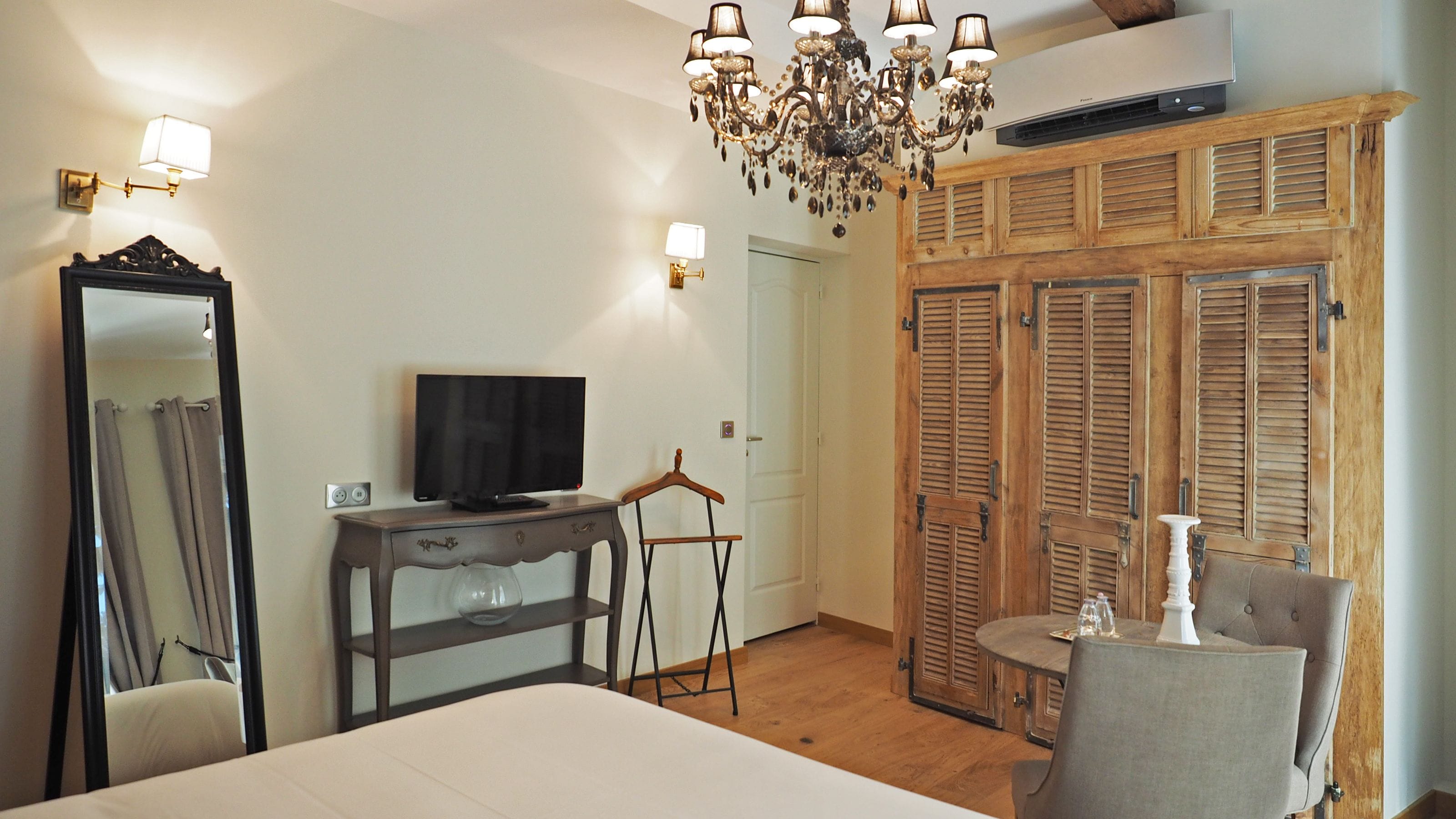 Une chambre à coucher avec un lit, une commode, un téléviseur, un miroir, un lustre et des volets en bois.