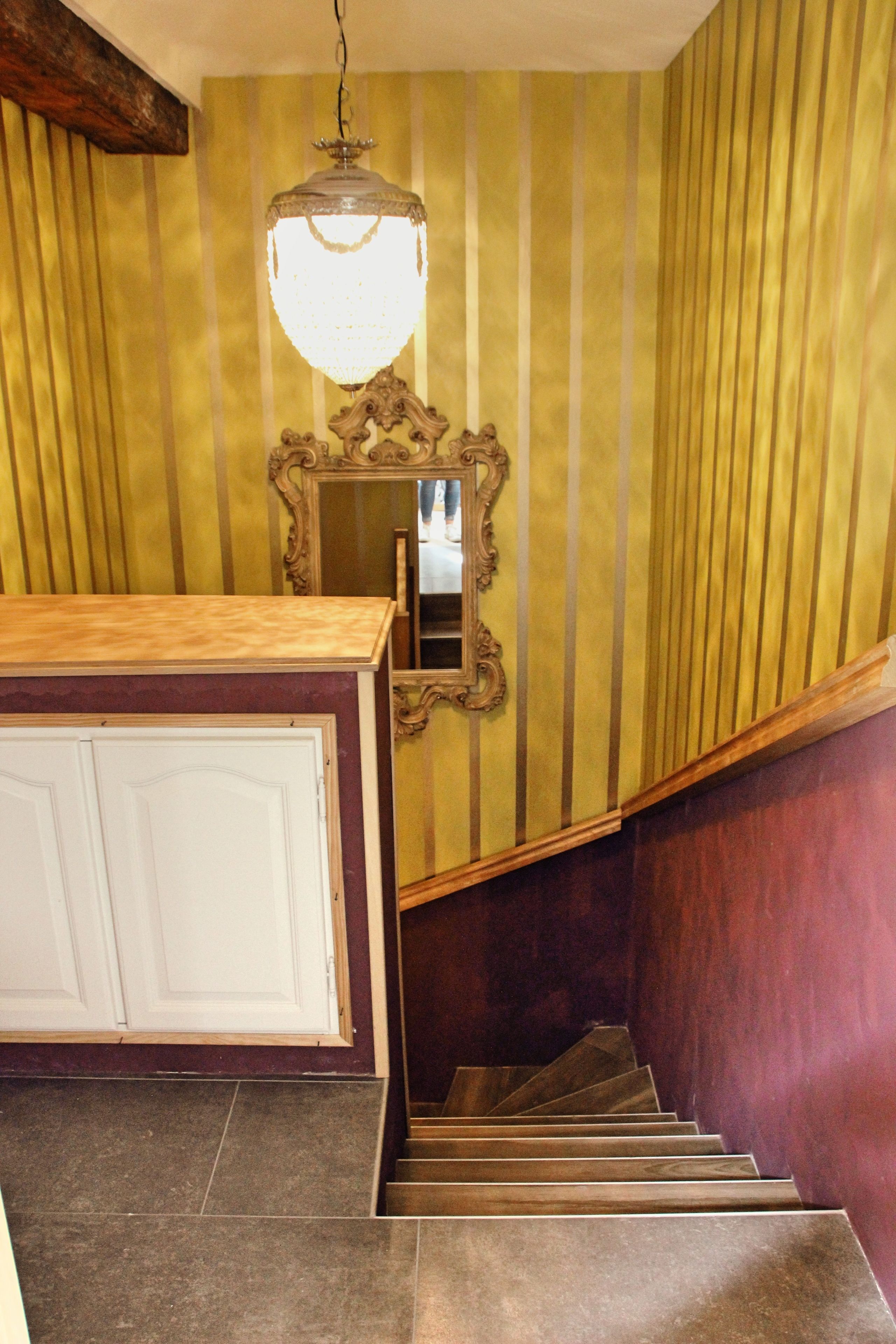 A staircase with a wooden handrail, a chandelier, and a mirror on the wall.