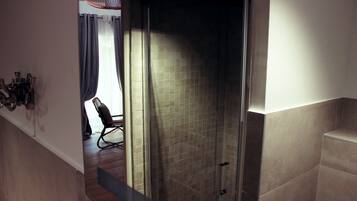 Un baño moderno con cabina de ducha de vidrio, paredes cubiertas de azulejos y una zona de estar con una silla y una mesa.