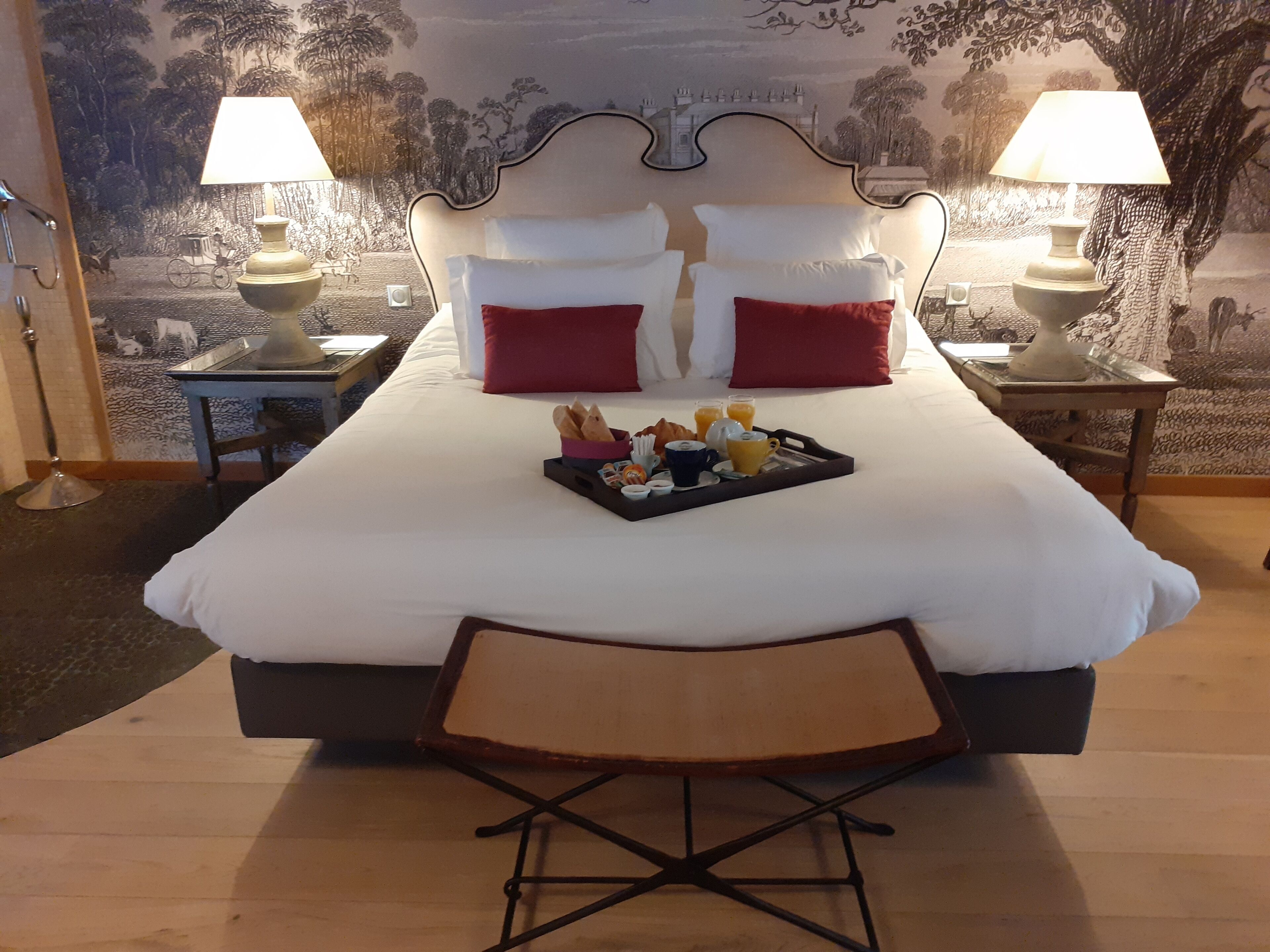 Una cama grande con almohadas blancas y rojas, una bandeja con alimentos para el desayuno y dos lámparas de noche.