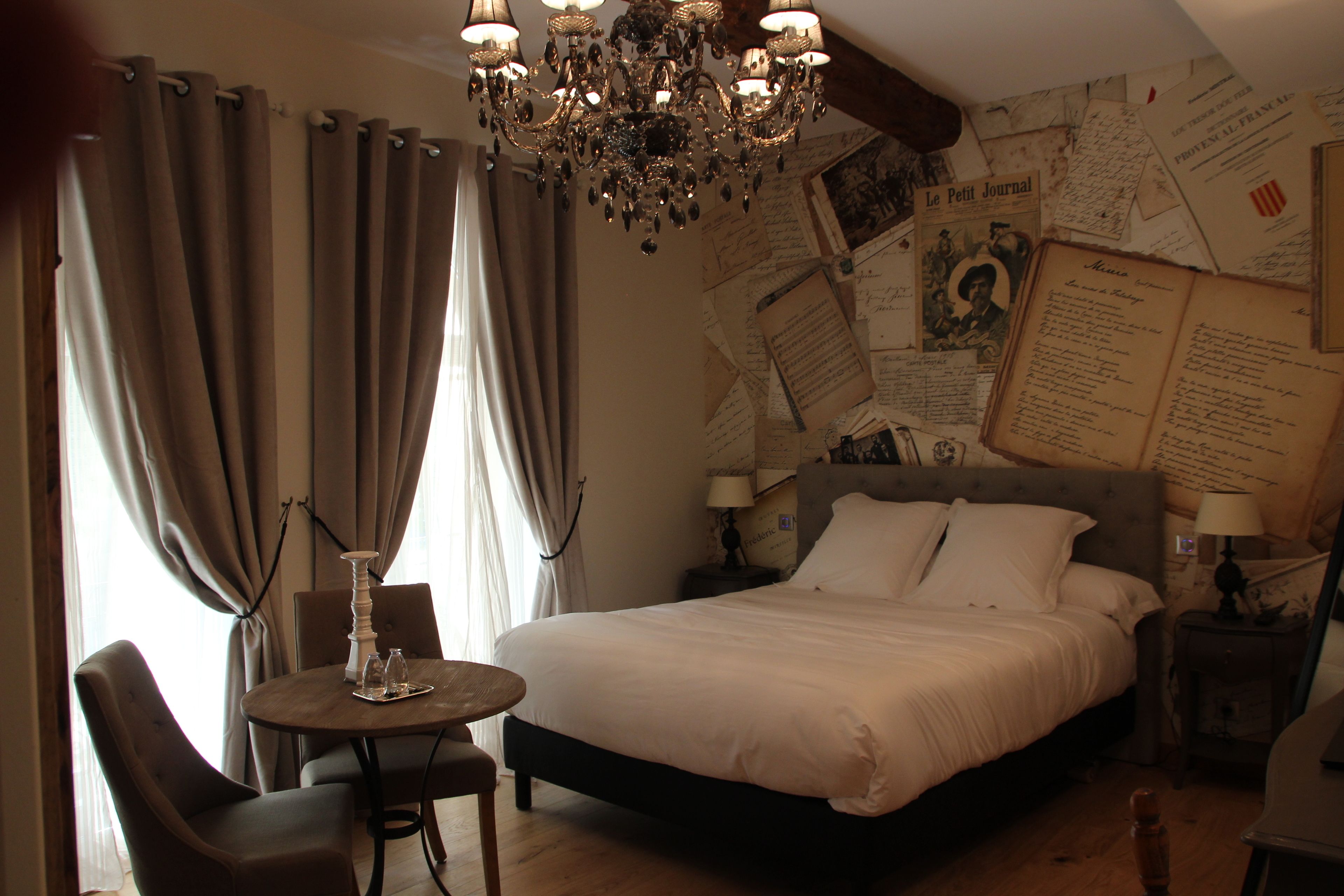 A bedroom with a large bed, a chandelier, a small table with chairs, and a wall covered with papers.