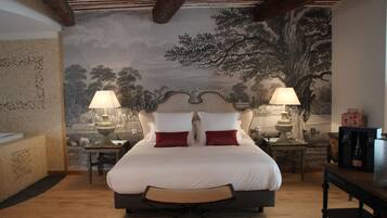 A bedroom with a large bed, two bedside tables with lamps, a wooden floor, and a mural on the wall.