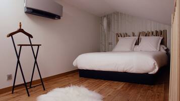 A bedroom with a bed, a wooden floor, a white fluffy rug, a wooden hanger, and a wall-mounted air conditioner.