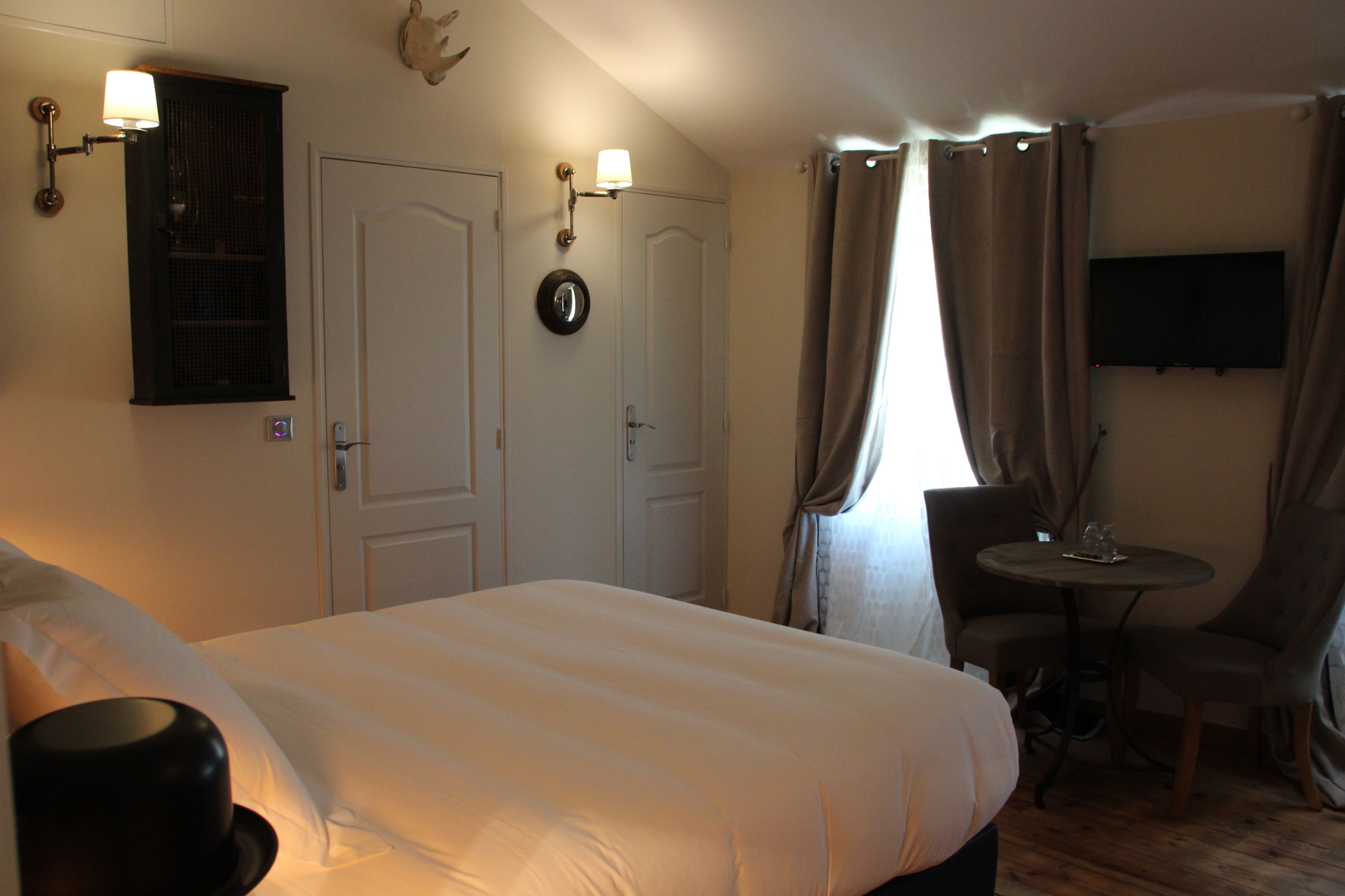 A hotel room with a large bed, a small round table with two chairs, a TV mounted on the wall, and a door with a light switch.