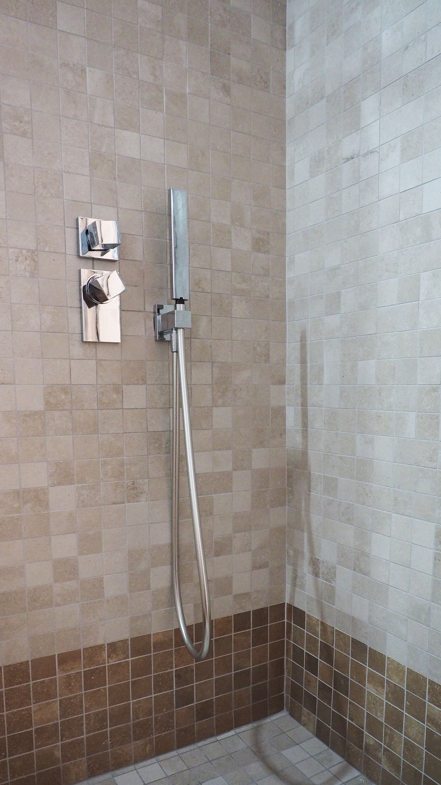 Un espace douche équipé d’un pommeau de douche à main et d’un panneau de commande fixé au mur.