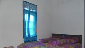 A room with a bed, a small table, and a window with a blue curtain. - Losmen Setia Kawan II (Ngadisari)